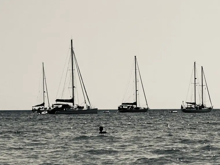 Le barche a vela all'ancora davanti alla spiaggia, in controluce.