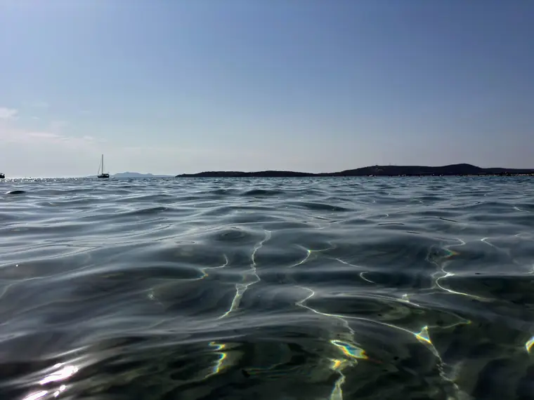 Il fondale sabbioso a pelo d'acqua e le barche all'ancora verso Capo Teulada.